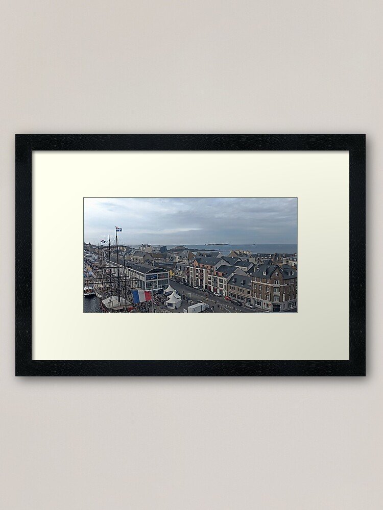 Panoramic view over the port of Saint-Malo with sailing masts, historic rooftops and the sea horizon under a soft cloudy sky in Brittany, France.